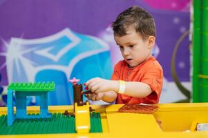 Close-up of a boy's child playing with colorful plastic bricks at a table. The kid has fun and builds from bright constructor cubes. Early learning. Educational toys photo