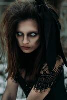 Portrait of a young woman in the Gothic gloomy image of a witch in a gloomy forest Halloween Costume. Vertical photo. photo