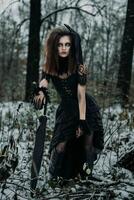 A scary female figure of a witch in a black robe in an autumn forest, an unsaturated image photo