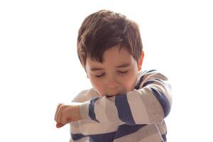 A boy sneezes or coughs into his elbow on white background. photo