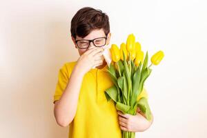 a boy with a bouquet tulips, covered his nose with a paper napkin and sneezes photo