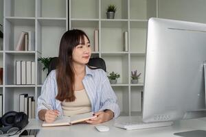 Young Student Studying Online at Home Using Desktop Computer in Modern Home Office Setting with Books and Plants photo