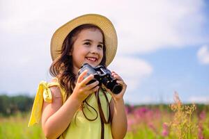 cute girl stands in a field with high grass against a blue sky in the summer, holds binoculars photo