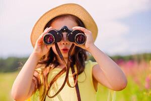 Surprised cute girl 4-5 years old in a straw hat looks through binoculars. photo