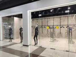 The window of an empty clothing store with black mannequins and empty hangers photo