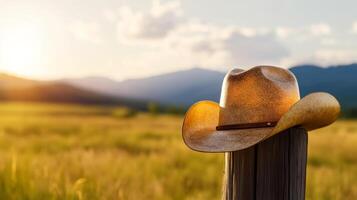 Close up of a weathered cowboy hat resting on a wooden fence post with a sunlit ranch in the background photo