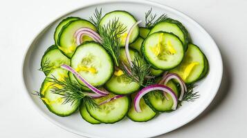 Top down view of a fresh cucumber salad with thin slices of cucumber red onion rings and dill on a white plate garnished with lemon zest on a white background photo