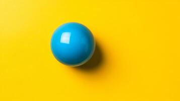 Isolated shot of a single bubble gum ball in bright blue centered on a vibrant yellow background with plenty of empty space photo