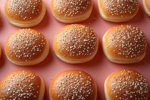 Freshly Baked Sesame Seed Hamburger Buns Arranged in Rows on a Pink Background photo