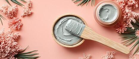 Natural Clay Face Mask with Wooden Applicator and Pink Floral Decorations on Peach Background photo