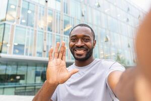 African American man with smartphone having call on street in city. Guy blogger streaming chatting in social network. Man having virtual meeting vlog online chat outdoor Selfie webcamera view photo