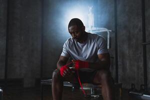 Fitness workout in gym. African American man fighter preparing for fight wrapping hands with red boxing wraps sports protective bandages in gym. Strong man ready for fight boxing sparring training photo