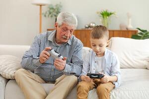 Happy family. Old senior man grandfather boy grandson playing game with joysticks at home. Smiling grandparent and child using gamepads for game. Older generation modern tech usage photo