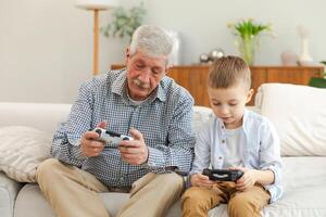 Happy family. Old senior man grandfather boy grandson playing game with joysticks at home. Smiling grandparent and child using gamepads for game. Older generation modern tech usage photo
