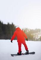 A man in a red jacket with a snowboard stands on a mountainside. photo