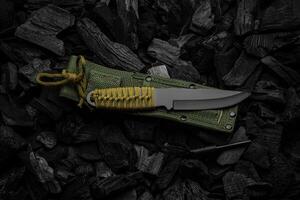 A modern knife with a black blade and a paracord-wrapped handle. Soft green scabbard. Dark charcoal back. photo