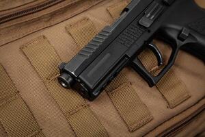 A modern black pistol on a brown military backpack. Weapons for defense and attack. Arming the police, army and special units photo