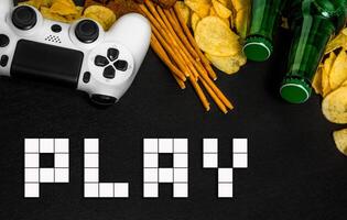 Modern white gamepad among chips, crackers and bottles of beer on a black. Game concept. photo