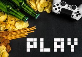 Modern white gamepad among chips, crackers and bottles of beer on a black. Game concept. photo