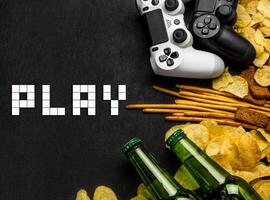 Modern white gamepad among chips, crackers and bottles of beer on a black. Game concept. photo