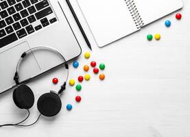 Notebook headphones, laptop and multi-colored sweets on a white background. Flat lay with copy space. photo