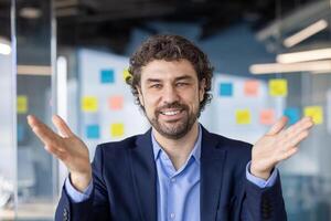 Confident businessman smiling and gesturing while talking during call in contemporary office. Casual conversation, connection, and successful communication concept photo