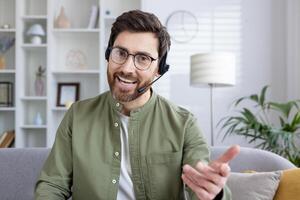 Smiling man wearing a headset and glasses, conducting an online meeting from his modern home office, explaining something enthusiastically. photo