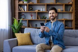Casual smiling man checking his smartphone while relaxing on a couch in a cozy living room setting. photo