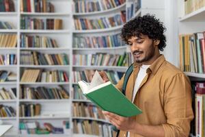 An adult male stands in a well-lit library, immersed in reading a green book. Bookshelves filled with various books surround him, suggesting a quiet atmosphere for study and literature exploration. photo