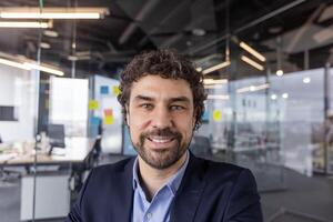 Confident businessman on call looking at camera in modern office. Professional setting with glass walls and contemporary lighting. Represents communication, work from home photo