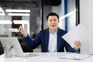 Frustrated male in formalwear looking at camera with despair while working with portable computer and stack of documents. Overloaded with paperwork employee not fitting in deadlines in office. photo