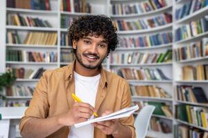Person in a casual jacket engaged in a call, holding a notebook in a library setting, signaling a learning or educational context. photo