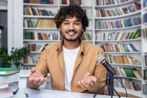 Focused individual recording a podcast at the library with a microphone and books in the background. photo