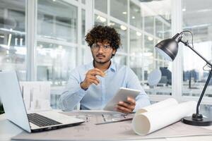 Architect working on a project in a modern office environment, using a digital tablet and architectural plans. photo