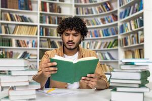 A diligent young man, deeply engrossed in reading a book, is surrounded by towering stacks of literature in a brightly lit university library. The concentrated ambiance highlights the seriousness of exam preparation and academic dedication. photo