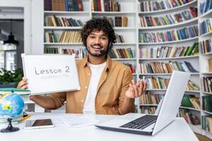 An enthusiastic online teacher giving a lesson from a home office with a whiteboard and a laptop in a bookshelf background. photo