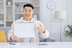 Happy man smiling and pointing at a blank whiteboard in a modern home office environment. Great for messaging, presentations, and promotional content. photo