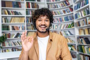 Cheerful student engaging in online learning, making a friendly gesture to the camera while using a headset in a library. photo