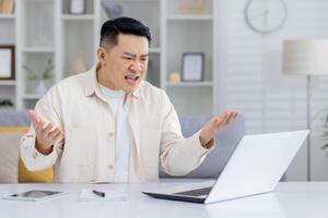 Man showing frustration and anger while looking at laptop in home office setting. Concept of technology issues, work stress, and negative emotions. photo