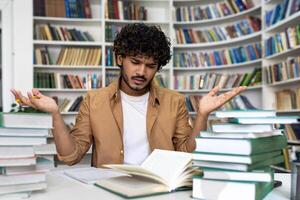Dissatisfied and frustrated student trying to concentrate and prepare for exam by himself, man sitting in library tired hard to study and learn material alone. photo