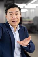 First person view of japanese man in business suit recording on frontal cam of smartphone on blurred background. Experienced male filming greeting material for educational materials. photo