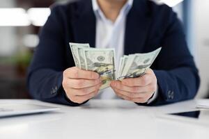 Close-up image of a businessman in suit holding dollar bills in his hands with an office environment in the background. photo