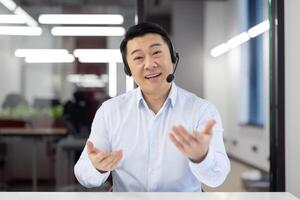 A cheerful Asian businessman in a headset actively engaging in conversation in an office setting. photo