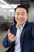 First person view of grown up japanese business person connecting to remote meeting and smiling to camera. Formal man wearing stylish suit while leading call with department of remote workers. photo