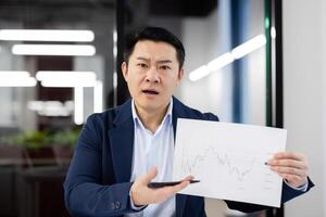 Worried businessman showing to camera paper with chart to camera with dissatisfied expression. Upset entrepreneur feeling frustrated with report about results of marketing department work. photo