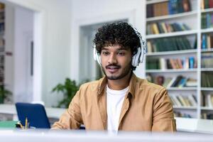 Serious concentrated man in headphones studying in library, hispanic student thinking and recording course while sitting in university campus library. photo