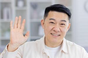 Friendly and cheerful man waving hello with a smile in a casual indoor environment. Perfect for concepts like communication, greeting, or friendship. photo