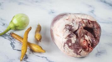 a raw heart on a marble counter with a knife and some vegetables photo