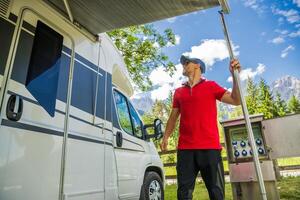 Man Setting up an Awning on an RV Camper Van in a Scenic Campground During the Day photo