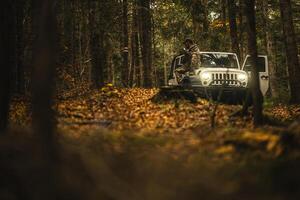 Hiker In Camouflage Enjoys Autumn Forest View Next To SUV In Late Afternoon Light photo